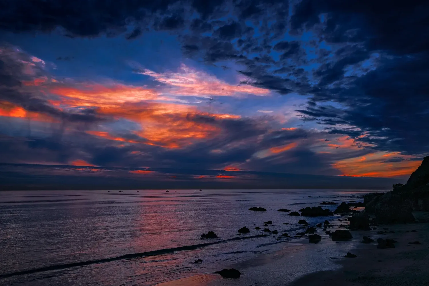 Malibu coastline at sunset with vibrant clouds and rocky beach
