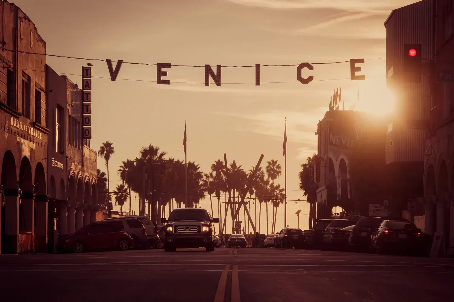 Venice Beach sign at sunset with palm trees and cars on the street